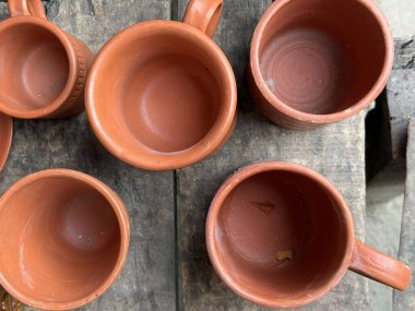 Tepeden bakıldığında, eski ahşap bir yüzey üzerinde düzgünce düzenlenmiş ve kırsal çömlek sergilenen el yapımı birkaç terracotta bardağı görülüyor..