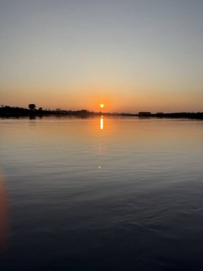 Gün batımında sakin sudan yansıyan dingin altın güneş ışığı, yüksek çözünürlüklü fotoğrafta huzur ve doğal güzellik sunuyor..