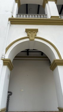 Zeytin yeşili mimari elementler ve dekoratif korkuluklar tarafından çerçevelenmiş geniş kemerli bir girişi olan büyük beyaz bir bina girişi..