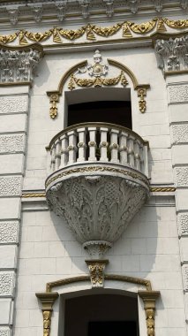 Çok güzel hazırlanmış beyaz bir balkonun detaylı bir çekimi. Özenle hazırlanmış altın süslemeler ve tarihi bir bina üzerindeki klasik balyalar..