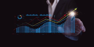 İş büyümesi ve veri analizi kavramı. Bir işadamı yükselen çubuklar ve eğilim çizgileriyle sanal bir finans tablosuna dokunarak başarıyı, karı, teknolojiyi ve dijital performans iyileştirmesini simgeliyor.