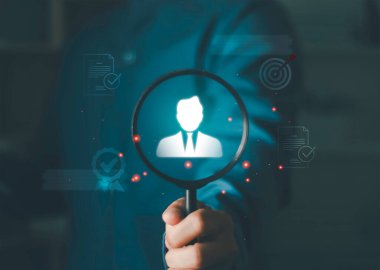 Mavi arka plandaki halk simgeleri arasında taçlandırılmış bir figüre odaklanan el ele tutuşan büyüteç, liderliği, işe almayı, insan kaynakları yönetimini ve en iyi performans gösteren potansiyel sanatçıyı sembolize ediyor..