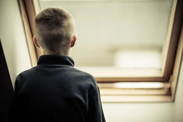 Jeune garçon solitaire regardant à travers la fenêtre en verre — Photo