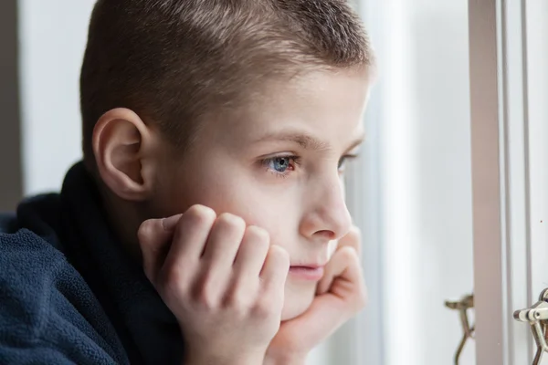 Pensive garçon se penche son visage sur les mains à la fenêtre — Photo