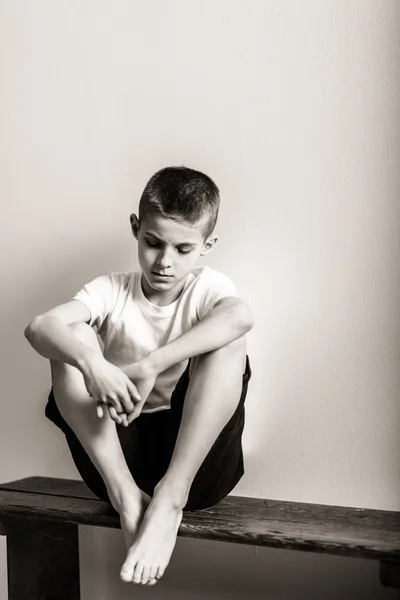 Одинокий мальчик, сидящий на скамейке с коленями — стоковое фото