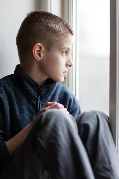 Niño huérfano solitario sentado en la ventana de vidrio — Foto de Stock