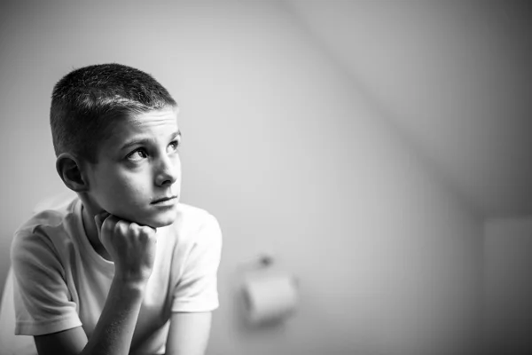 Созерцательный мальчик сидит на унитазе в монохромном — стоковое фото
