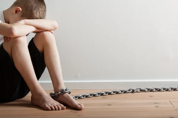 Solitario ragazzo con catena su il suo piede nascondendo la sua faccia — Foto Stock