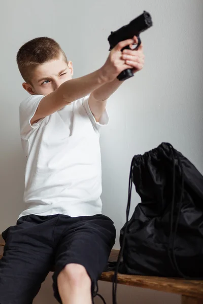 Ung pojke satt på en bänk pekar en pistol uppåt — Stockfoto