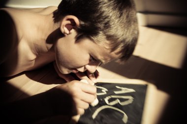 Cute boy writing a,b and c on chalk board clipart