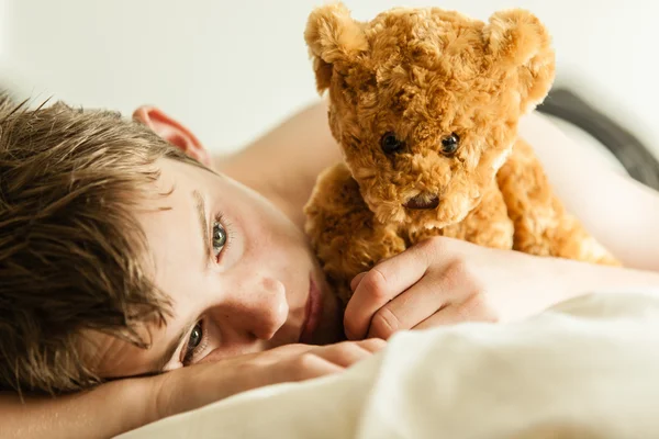 Tiener jongen knuffelen op bed met bruine Teddy beer — Stockfoto
