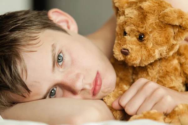 Adolescent garçon nichant sur lit avec brun ours en peluche — Photo