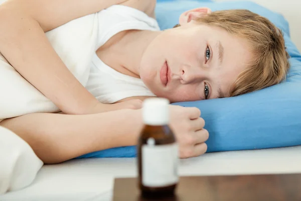 Ill bambino maschio sdraiato accanto al flacone del medicinale — Foto Stock