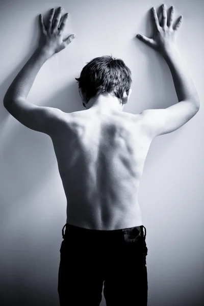 Black and white back of teen with hands on wall