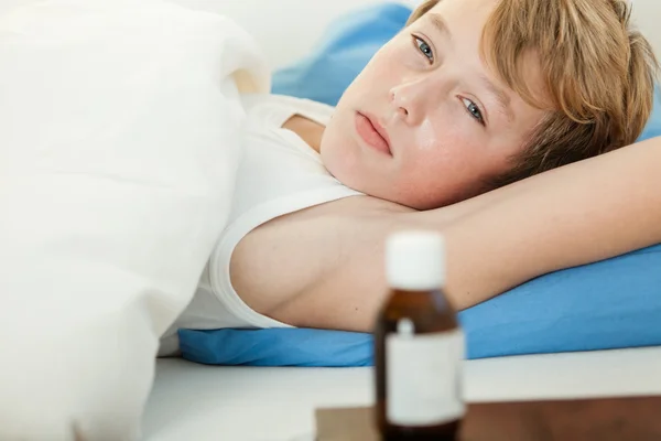 Febbre ragazzo a letto accanto alla bottiglia medicina — Foto Stock