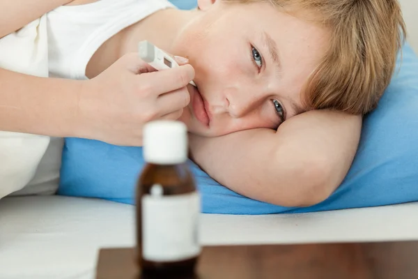 Ragazzo che utilizza termometro con bottiglia di medicina nelle vicinanze — Foto Stock