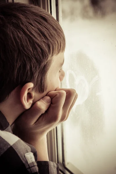 Boy looking out window with heart icon on glass — Stock Photo, Image