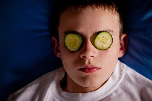 Niño en la cama con rodajas de pepino sobre sus ojos — Foto de Stock