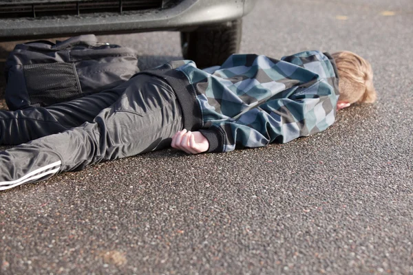 Пострадавший в автомобильной аварии мальчик лежит на дороге на автомобиле — стоковое фото