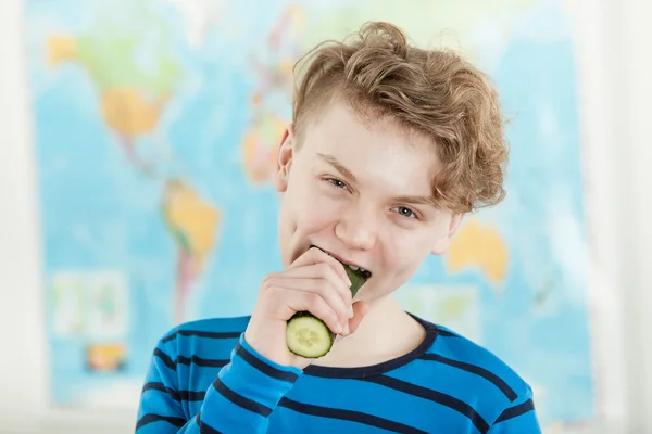 Menino adolescente comendo pepino inteiro na frente do mapa — Fotografia de Stock