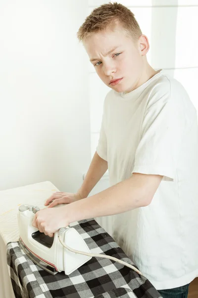 Мальчик гладит рубашку и смотрит сердито — стоковое фото