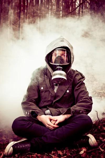 Boy in gas mask with crossed legs in front of fog — Stock Photo, Image