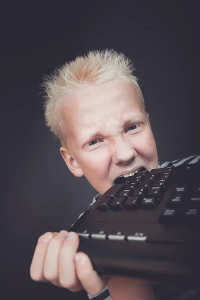 Rapaz irritado com cabelo loiro segurando teclado — Fotografia de Stock
