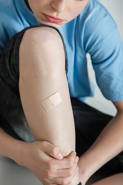 Niño con vendaje que cubre la herida en la espinilla — Foto de Stock