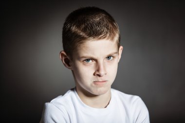Angry male child posing pensively in dark room clipart