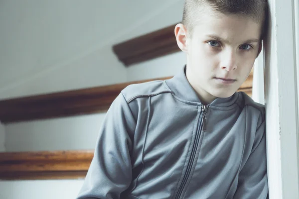 Serious lonely boy in gray jacket beside staircase — Stock Photo, Image