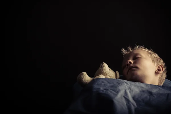 Menino com urso de brinquedo dormindo no quarto escuro — Fotografia de Stock