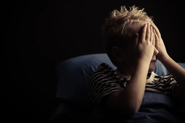 Niño cubriendo los ojos mientras yacía en la cama — Foto de Stock