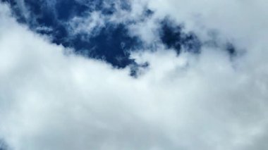 Görüntü görüntülerinde parlak, mavi gökyüzüne dağılmış tüylü beyaz bulutlar görülüyor. Gökyüzü masmavi ve güneş ışığı altında aydınlanıyor..