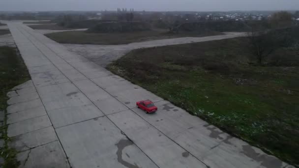 Červené auto na prázdné betonové silnici v oblačný podzimní den — Stock video