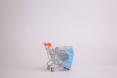 Karantina konseptiyle güvenli ve online alışveriş. Koronavirüse karşı koruyucu tıbbi maskeli alışveriş arabası. Beyaz arkaplan, alanı kopyala.