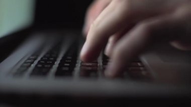 Karanlık odadaki klavye dizüstü bilgisayarında çalışan tanınmayan hacker programcısının aşırı yakın çekim elleri.