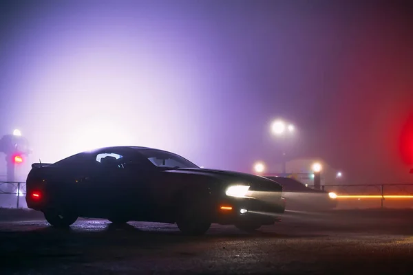 Sport car in the shadows with glowing lights in low light at foggy night, or silhouette of sport car dark background. Selective focus — Stock Photo, Image