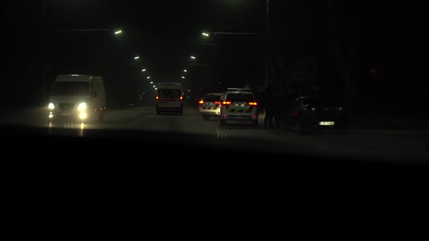 Две полицейские машины с ослепляющим светом стоят на дороге. Вид из бегущей машины. — стоковое видео