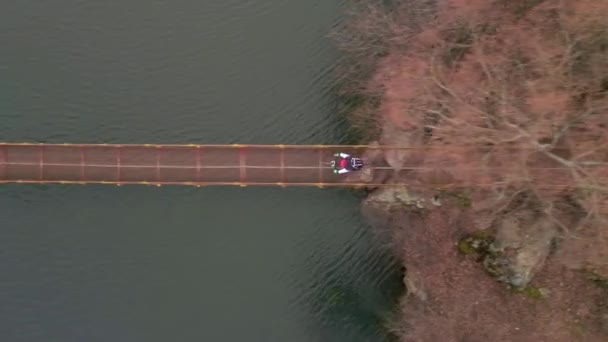 Aerial rallentatore colpo di giovane sportivo cavalca in bicicletta sul ponte sospeso sul piccolo fiume in primavera giorno. Buone vacanze o allenamento nella nuvolosa giornata primaverile. Stile di vita ciclistico sano — Video Stock