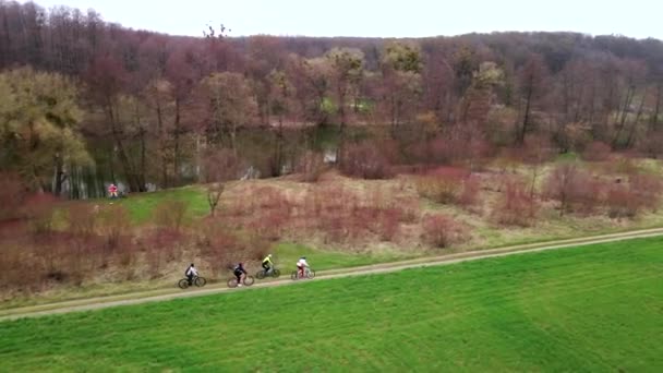 Воздушный кадр юношей на велосипедах по проселочной дороге возле зеленого поля в весенний облачный день. Здоровый образ жизни — стоковое видео