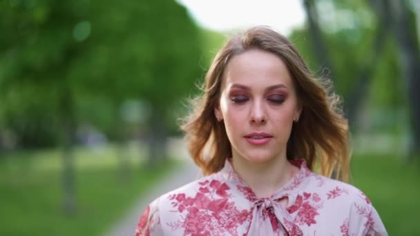 Aantrekkelijke jonge vrouw met rokerige ogen make-up blik op camera glimlach staan in het stadspark slow motion — Stockvideo