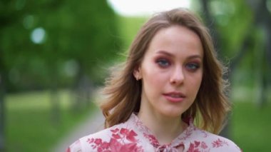 Çekici, dumanlı gözlü genç kadın kameraya bak gülümse. Şehir parkında ağır çekimde dur.