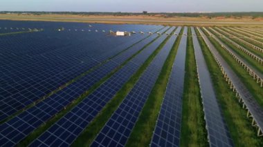Güneşli bir yaz akşamında güneş çiftliğindeki büyük güneş panellerine hava aracı görüntüsü. Güneş pili santralleri, yeşil çimenler. Görüntü 4k.