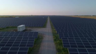Güneşli bir yaz akşamında güneş çiftliğindeki büyük güneş panellerine hava aracı görüntüsü. Güneş pili santralleri, yeşil çimenler. Görüntü 4k.