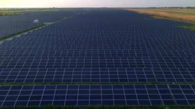 İnsansız hava aracı, güneşli bir yaz akşamında güneş panellerinin üzerinden uçar. Güneş pili santralleri, yeşil çimenler. Görüntü 4k.