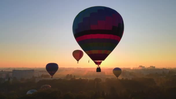 Drohnenbild Silhouette eines bunten Heißluftballons, der bei Sonnenaufgang über dem grünen Park in einer kleinen europäischen Stadt fliegt. HDR-Video — Stockvideo