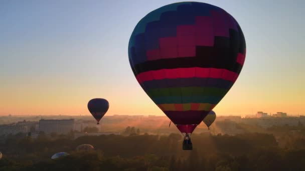 Drohnenbild Silhouette eines bunten Heißluftballons, der bei Sonnenaufgang über dem grünen Park in einer kleinen europäischen Stadt fliegt. HDR-Video — Stockvideo