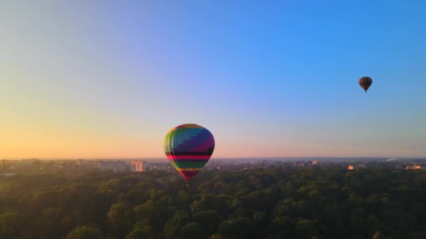 Drohnenbild Silhouette eines bunten Heißluftballons, der bei Sonnenaufgang über dem grünen Park in einer kleinen europäischen Stadt fliegt. HDR-Video — Stockvideo