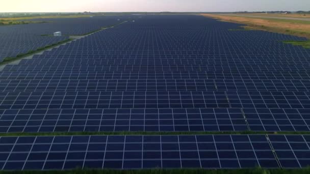 Drone primer plano vuela sobre grandes paneles solares en una granja solar en la soleada noche de verano. Plantas de energía solar, hierba verde. Vídeo de archivo 4k. — Vídeo de stock
