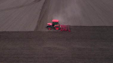 Tarlada tarla süren tarımsal kırmızı küçük traktör, tarlada çalışıyor. Sahada çalışan bir traktörün üzerinden uçmak. Traktör, alanın havadan yavaş çekim görüntüsünü sürüyor.